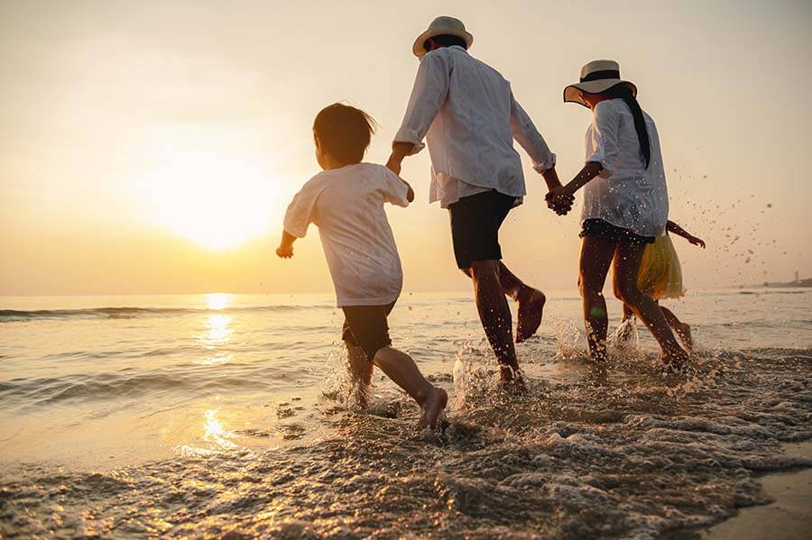 Familie geht bei Sonnenuntergang durch flaches Meerwasser an der Küste