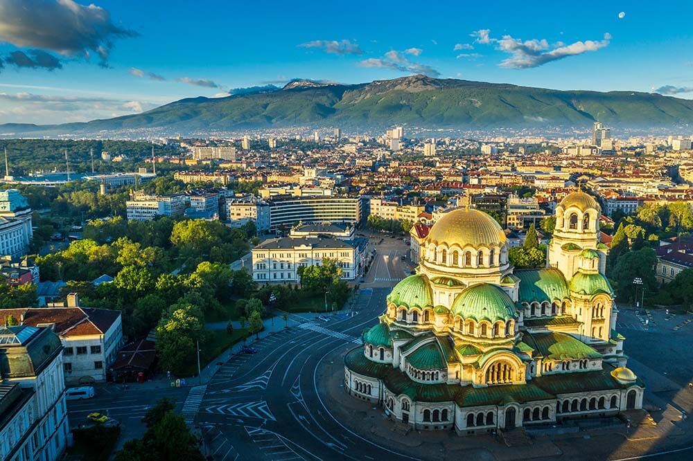 Luftaufnahme von Sofia mit goldenen Kuppeln der Alexander-Newski-Kathedrale und bergigem Hintergrund mit Stadtbild