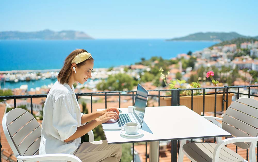 Fernarbeit bei der Bewertung des bulgarischen Wohnkomforts Frau arbeitet per Fernzugriff an ihrem Laptop von einer malerischen Terrasse mit Blick auf die bulgarische Küstenstadt und bewertet den Wohnkomfort