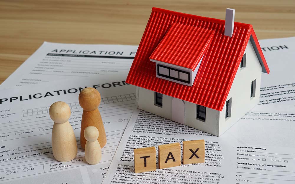 Optimierung der Besteuerung von Immobilienverkäufen für EU-Bürger Modell eines Hauses mit rotem Dach mit hölzernen Steuerwürfeln und Dokumenten zur Veranschaulichung der Optimierung der Besteuerung des Immobilienverkaufs für EU-Bürger